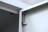 Close-up view of a metal spring mechanism on a white cabinet or locker. Produktbild-Vorschau
