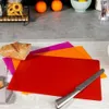 A set of three flexible cutting mats in red, orange, and purple, with a loaf of bread on top, and a knife on the red mat. Voir les images du produit