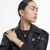 A woman wearing a black leather jacket and jewelry, including bracelets, earrings, a necklace, and a brooch. The jewelry features apple motifs and the 'I Love NY' slogan. Anteprima dell’immagine prodotto
