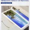 A printed image of a tropical beach scene with palm trees is being fed into a printer. Produktbild-Vorschau