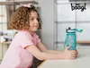 A young girl is sitting at a table, holding a water bottle. Podgląd zdjęcia produktu