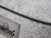 A close-up view of a grey dog bed with a black trim and a leather patch with a dog logo and the brand name 'DOGGYDOG'. Produktbild-Vorschau