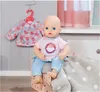 A baby doll is sitting on a pink box with a polka dot pattern, wearing a pink t-shirt and blue jeans. A floral patterned jacket is hanging on a pink hanger in the background. Podgląd zdjęcia produktu