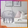 A macrame hanging chair is shown in a cozy room setting with pillows and artwork on the wall. Voir les images du produit