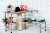 A stainless steel corner shelf unit with various kitchen items on it, including jars, a pitcher, and a small potted plant. Anteprima dell’immagine prodotto