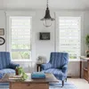 A living room scene with two chairs, a coffee table, and windows with blinds. Produktbild-Vorschau