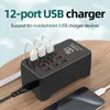 A black 12-port USB charger station with multiple white USB cables plugged in, placed on a wooden surface with a smartphone in the foreground. Náhled obrázku produktu