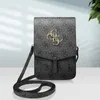 A grey Guess handbag with a repeating logo pattern and gold hardware, displayed against a light background with a hint of greenery. Podgląd zdjęcia produktu