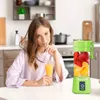 A woman is drinking juice at a table next to a portable blender filled with fruit. Náhled obrázku produktu