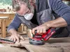 A man is sanding a piece of wood with a power sander in a workshop. Produktbild-Vorschau