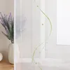A close-up of a sheer white curtain with green embroidered wavy lines and beads, next to a vase of lavender. Produktbild-Vorschau