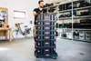 A man is pushing a stack of black storage boxes on a trolley in a workshop or garage setting. Náhled obrázku produktu
