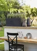 A black rectangular planter filled with lavender sits on a ledge next to a black watering can and a decorative object. Below, a wooden table is set with a chair and decorative items. Náhľad obrázku produktu