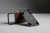 A brown leather phone case and a black magnetic accessory are displayed on a gray surface with a dark gray background. Produktbild-Vorschau