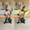 A woman is shown exercising on a stationary bike in two different positions, with a large arrow indicating movement or progression. Produktbild-Vorschau