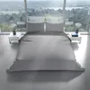 A bed with gray bedding is set up in a modern room with large windows overlooking a landscape. Produktbild-Vorschau