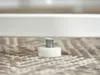 A close-up of a furniture leg with an adjustable foot on a textured rug. Podgląd zdjęcia produktu