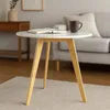 A round white coffee table with bamboo legs is placed on a rug in a living room setting. A book and a mug are on the table, and a sofa is visible in the background. Podgląd zdjęcia produktu