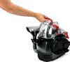 A hand is shown holding the handle of a portable carpet cleaner. Voir les images du produit