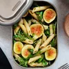 A close-up view of a lunchbox filled with pasta salad, figs, and greens. Podgląd zdjęcia produktu