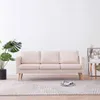 A cream-colored three-seater sofa is shown in a well-lit room with a plant and a small side table. Náhled obrázku produktu