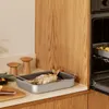 A roasted fish in a roasting pan on a kitchen counter next to wooden salt and pepper grinders. Náhled obrázku produktu