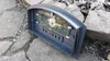 A pizza oven door with a glass window and thermometer, lying on a stone surface. Produktbild-Vorschau