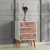A white and wood-effect chest of drawers with three drawers, decorated with patterned panels and wooden knobs. A vase with purple flowers sits on top. The chest of drawers is placed against a grey paneled wall. Produktbild-Vorschau