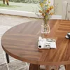 A close-up view of a round wooden dining table with a vase of flowers and a magazine on it, set in a well-lit room with a window in the background. Podgląd zdjęcia produktu