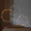 Three illuminated LED wreaths hang in a room, with a brown curtain in the background and a wooden table in the foreground. Produktbild-Vorschau