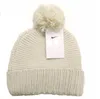 A cream-colored knitted beanie with a pom-pom on top and a Nike tag attached. Voir les images du produit