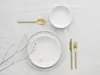A minimalist table setting with white plates and gold cutlery. Produktbild-Vorschau