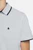 Close-up of a person wearing a light gray polo shirt with black trim on the collar and sleeves. A small black logo is visible on the chest. Produktbild-Vorschau