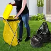 A person is shown using a yellow trash bag holder with a lid in a grassy outdoor setting. Two black trash bags are also visible. Anteprima dell’immagine prodotto