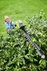 A woman is using a hedge trimmer to trim a bush in a garden. Produktbild-Vorschau