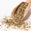 A wooden scoop filled with dried mate tea leaves and stems, with some spilled onto a white surface. Produktbild-Vorschau