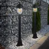 Two black outdoor lamps are placed in front of a gabion wall filled with stones, with a curb and road visible in the foreground. Produktbild-Vorschau