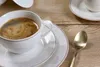 A close-up of a cup of coffee on a wooden table, with a spoon and saucers. Produktbild-Vorschau