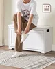 A person sits on a white storage bench, tying their shoes. Produktbild-Vorschau