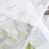 A close-up view of a transparent fabric with a white wave pattern embroidery, showing green apples inside. Produktbild-Vorschau