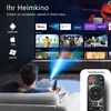 A person is sitting on a couch watching a movie projected from a mini-projector onto a large screen. The screen displays various streaming service logos and movie posters. Produktbild-Vorschau