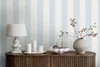 A still life arrangement on a wooden cabinet, featuring a lamp, candles, a bowl of pears, and a vase with branches, set against a striped blue and white wallpaper. Produktbild-Vorschau