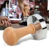 A close-up shot of a coffee tamper with a wooden handle, with a blurred background of a coffee shop setting. Náhled obrázku produktu