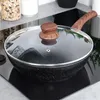 A black frying pan with a glass lid and a wooden handle sits on a black induction stovetop. Produktbild-Vorschau
