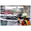 A firefighter uses a reciprocating saw to cut through a car windshield during a rescue operation. Fire trucks are visible in the background. Anteprima dell’immagine prodotto