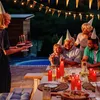 A family is celebrating a birthday outdoors at night, with a cake and candles. Produktbild-Vorschau