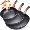 Three frying pans of different sizes are stacked on a white background. The top pan has a fried egg, bacon, and tomatoes floating above it, suggesting food preparation. Náhled obrázku produktu