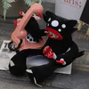 A black monster plush toy with red mouth and white eyes is sitting on a newspaper next to a pink rotary phone. Another smaller black plush toy is in front of it. Produktbild-Vorschau