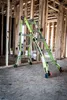 A green Little Giant ladder is set up inside a house under construction, with wooden studs visible in the background. Podgląd zdjęcia produktu