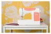 A white sewing machine sits on a white table in front of a yellow floral wallpaper. Anteprima dell’immagine prodotto